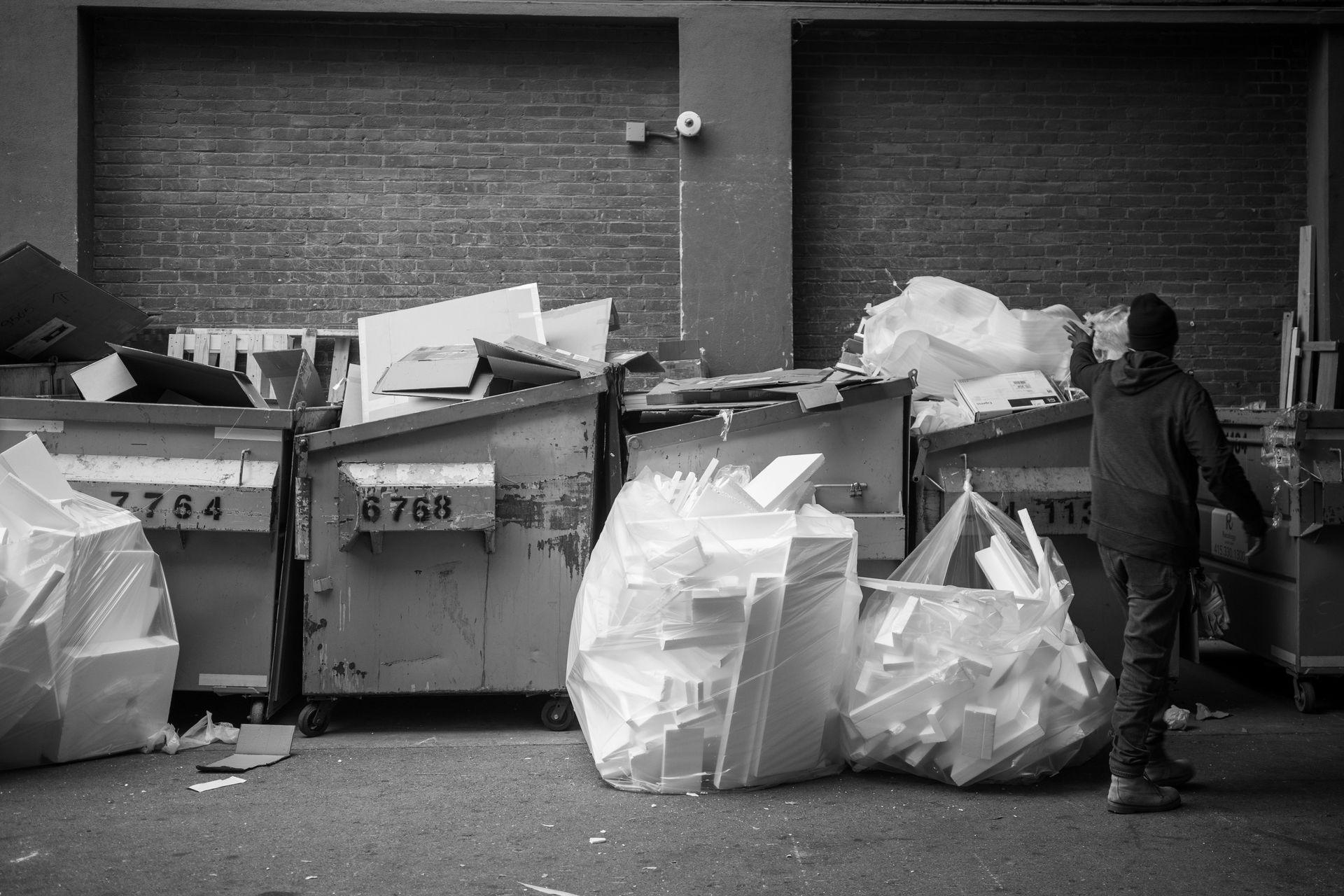 Person standing near dumpsters filled with trash bags